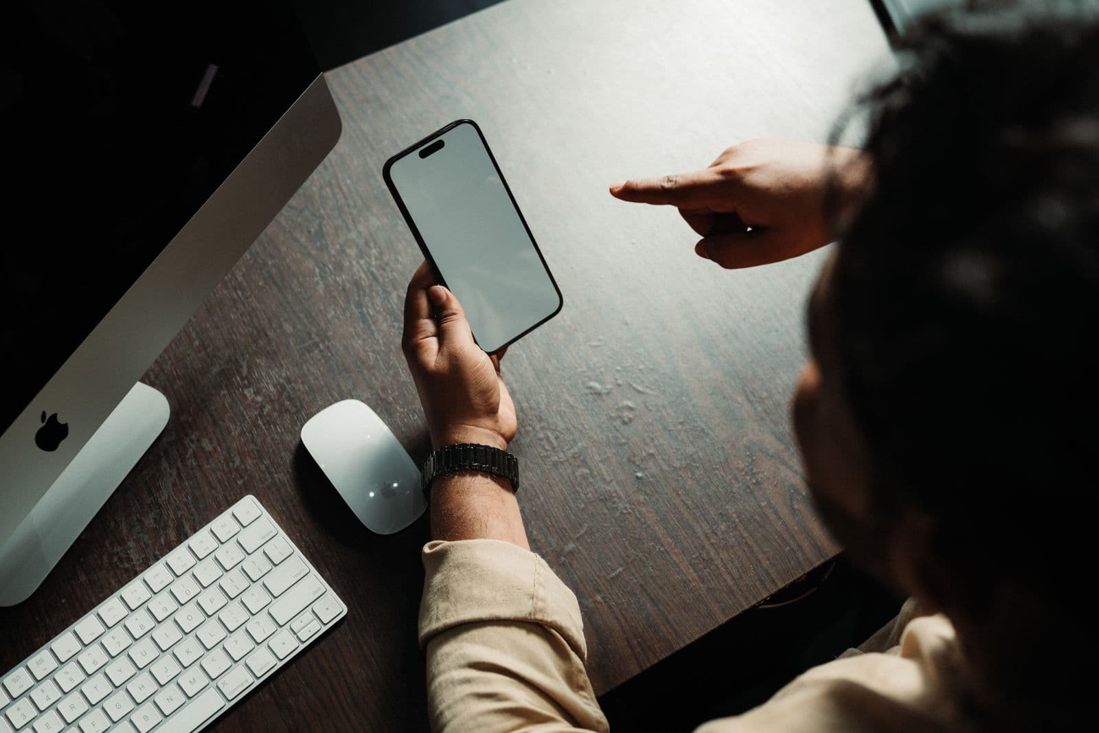 Person holding an iPhone while seated at a desk with a computer
