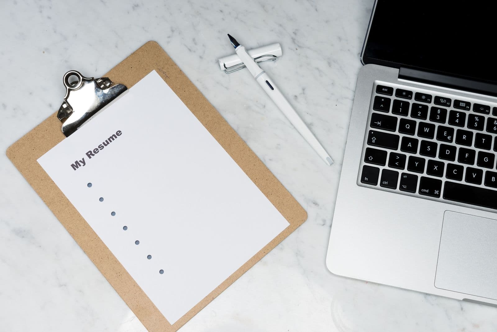 Resume on a clipboard beside a pen and open laptop
