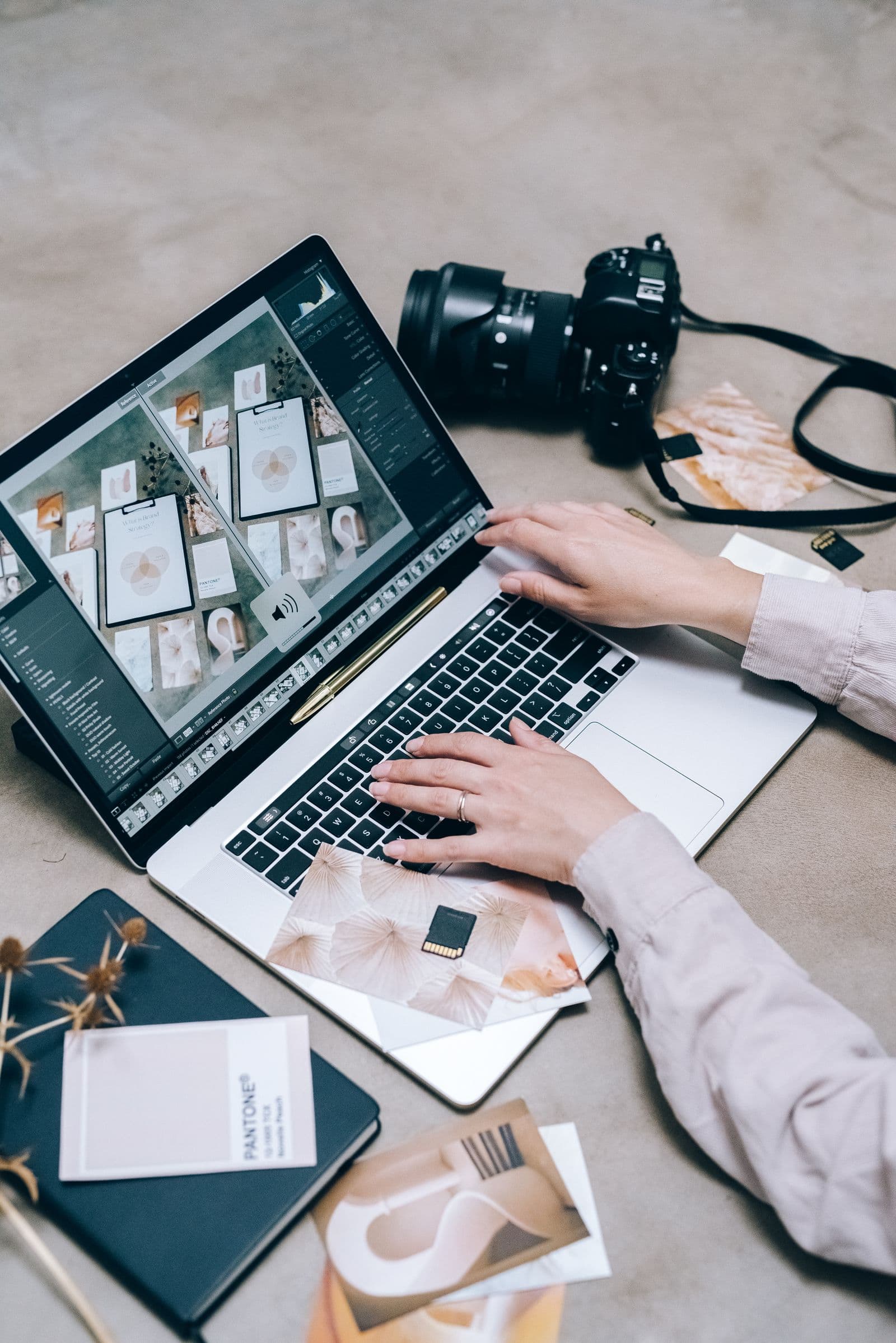 Close-up of hands editing photos on a laptop next to a camera